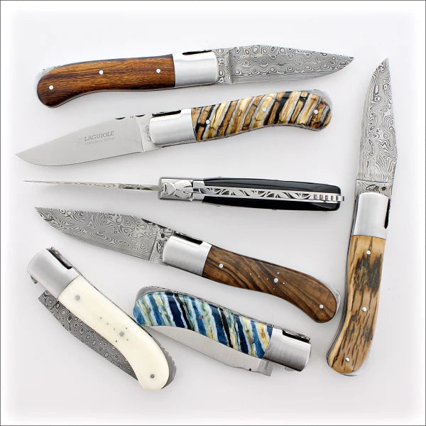 several Laguiole Gentleman folding knives Mammoth Damascus & Tooths on a white background