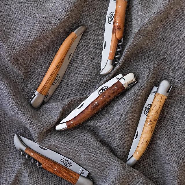 five laguiole knives with wooden handles folded on top of a grey cloth.