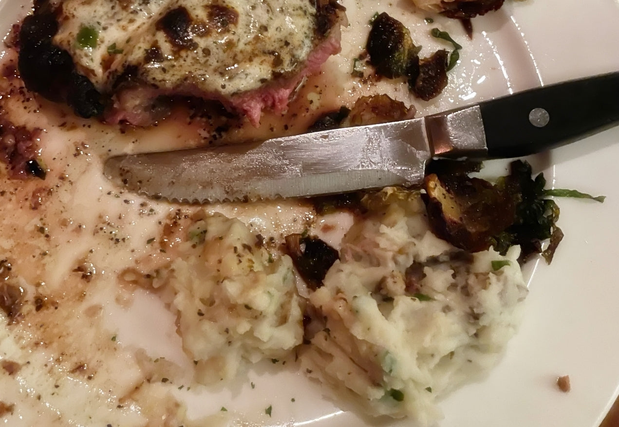 Big steak knife with teeth on a plate next to a steak. 