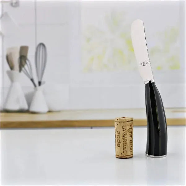 a horn tip butter spreader by Forge de Laguiole. The spreader stand vertically on the widest part of the horn. this spreader is made of black horn tip