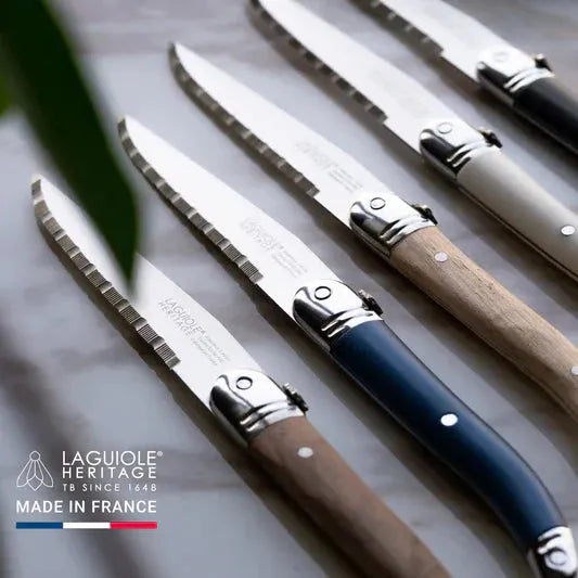 five laguiole heritage steak knives on a table. colors are starting from the bottom - dark brown, blue, light brown, white, black