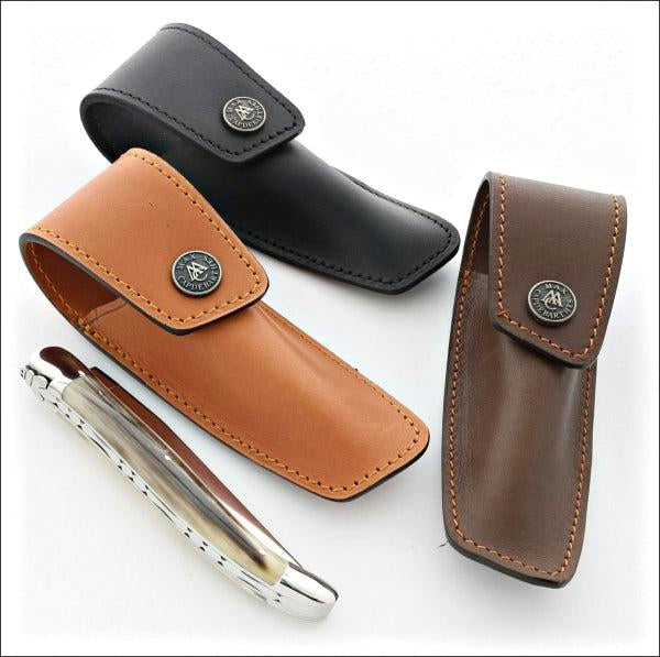 3 leather sheaths. a light brown a dark brown and a black with a laguiole knife in the foreground