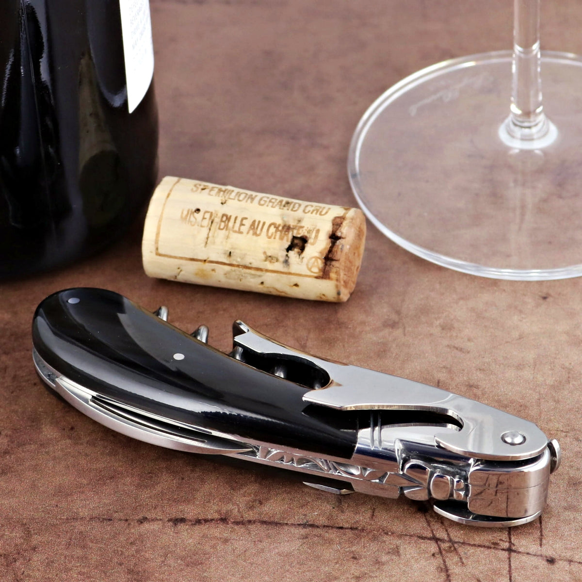 Laguiole Magnum Black Horn Tip Corkscrew, side view, with wine bottle, cork, and glass.