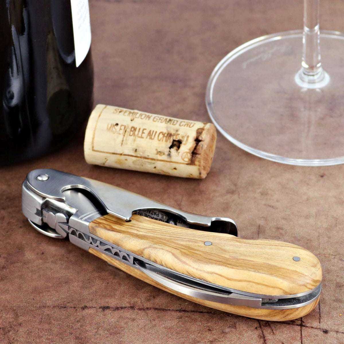 Laguiole Magnum Olive Wood Corkscrew, close-up of handle with wood grain, wine bottle, cork, glass.