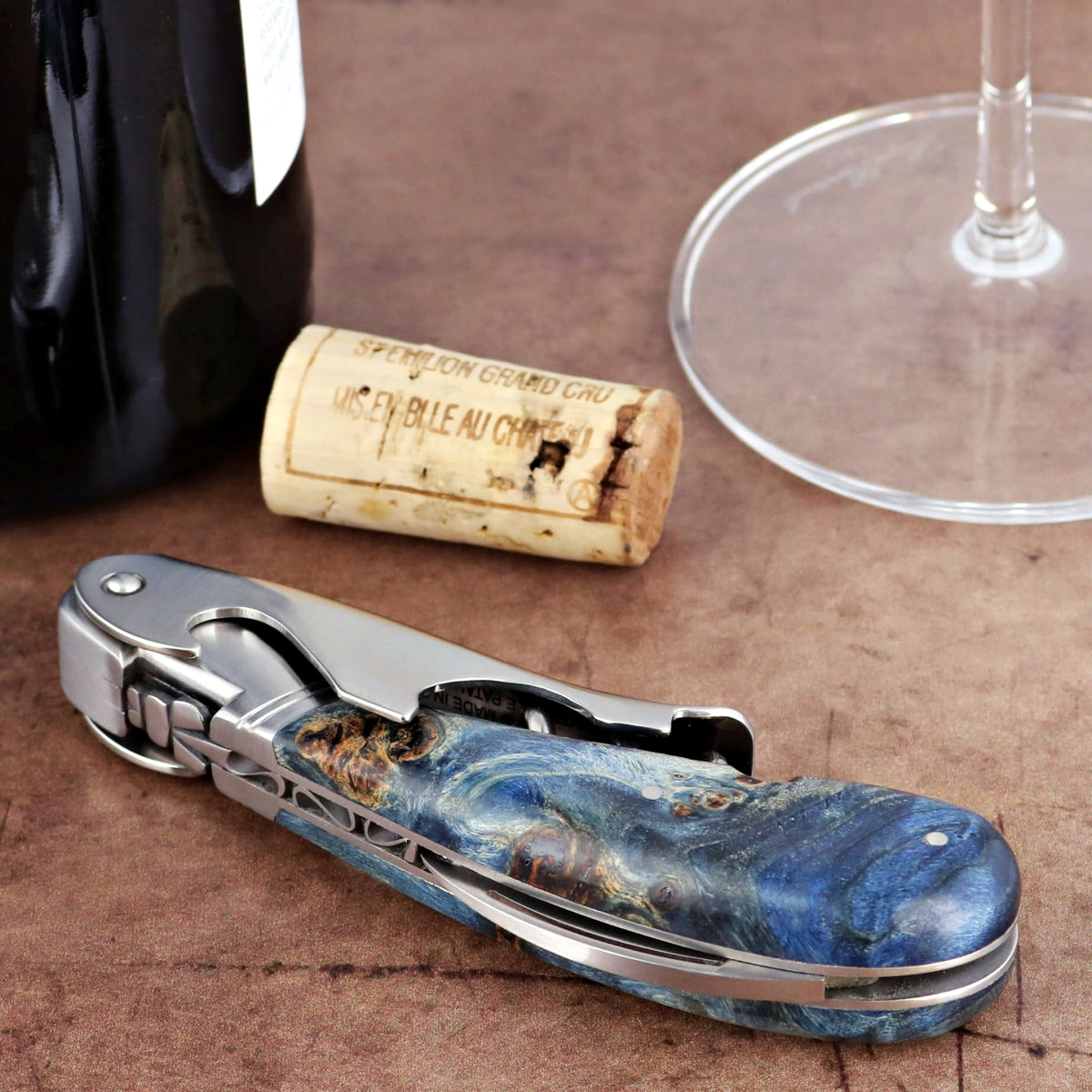 Laguiole Magnum Blue Stained Poplar Burl Corkscrew, close-up of handle with wine bottle and cork.