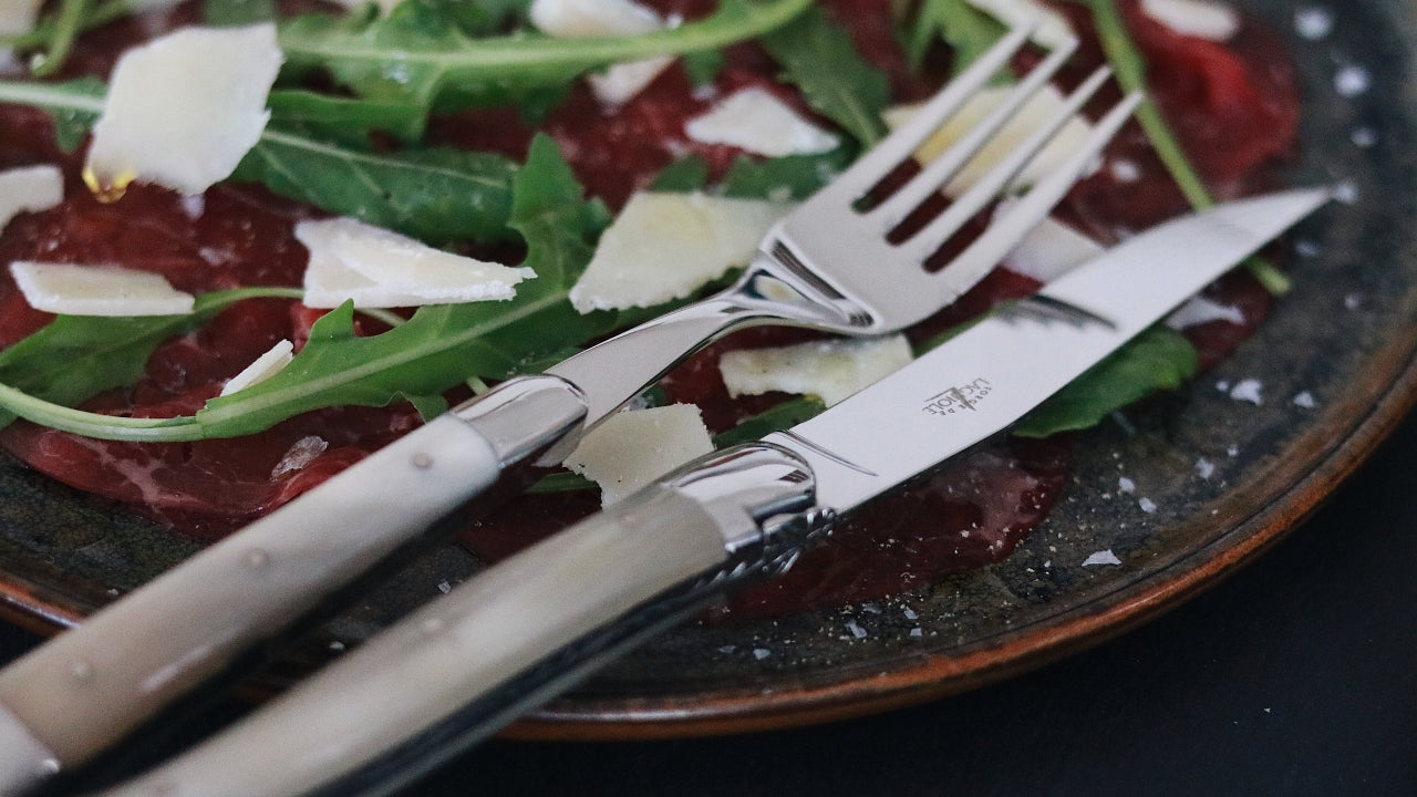 a forge de laguiole fork and knife with light horn handle on a plate with salad