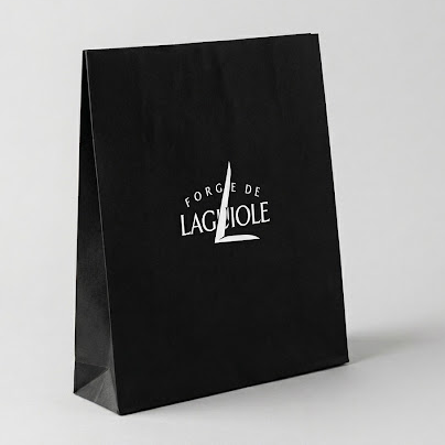 A black paper shopping bag with a white printed logo reading 'FORGE DE LAGUIOLE' on a light gray studio background.