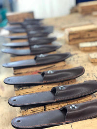several brown leather sheaths and a wooden bench awaiting to be completed
